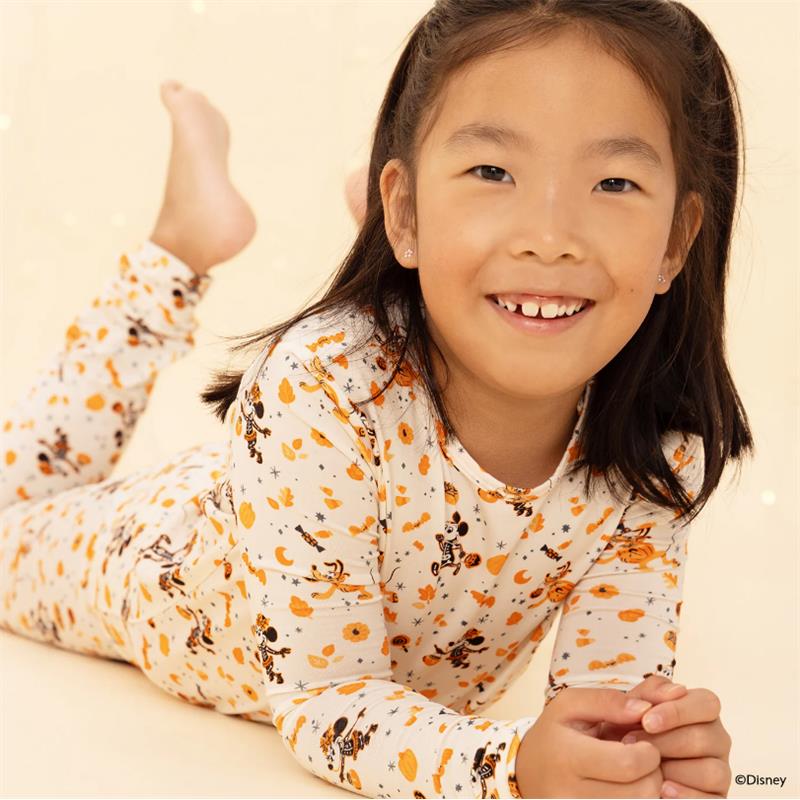 A smiling child in a white long sleeve pajama set with Halloween-themed prints, lying on her stomach.
