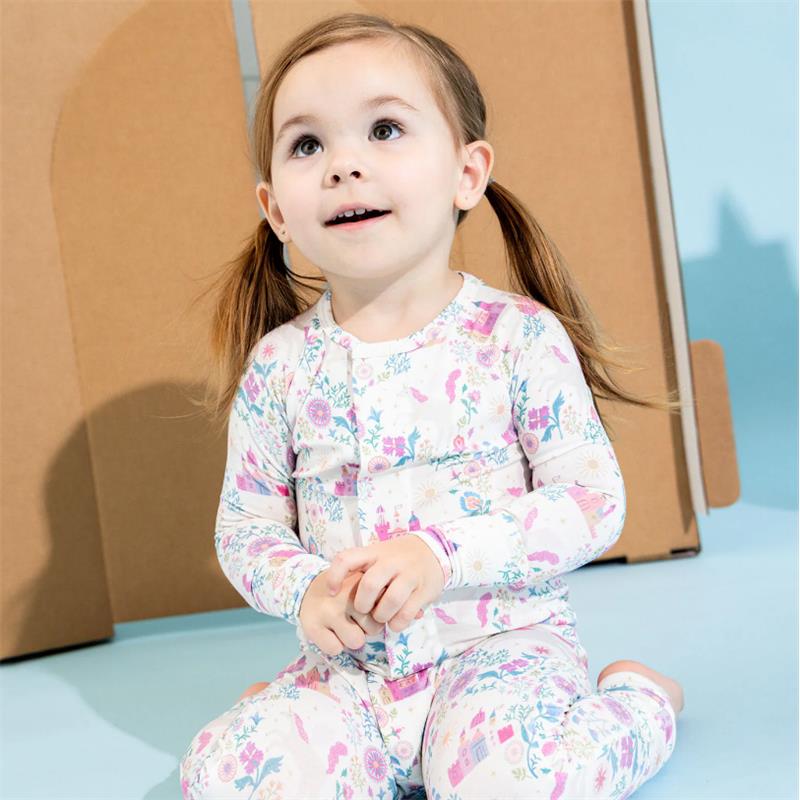 Toddler sits smiling in a colorful floral modal convertible coverall with buttons, on a blue background.