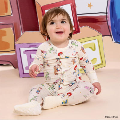 Baby wearing a Toy Story-themed modal coverall featuring characters like Woody and Jessie, sitting against a colorful block backdrop.