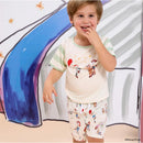 Child wearing a Toy Story-themed short sleeve shirt and shorts featuring Woody and friends, smiling in a colorful setting.