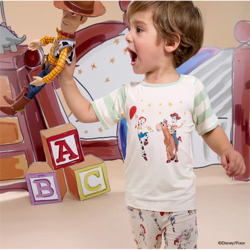 Child in a Toy Story-themed short set, excitedly holding a Woody action figure, with colorful blocks in the background.