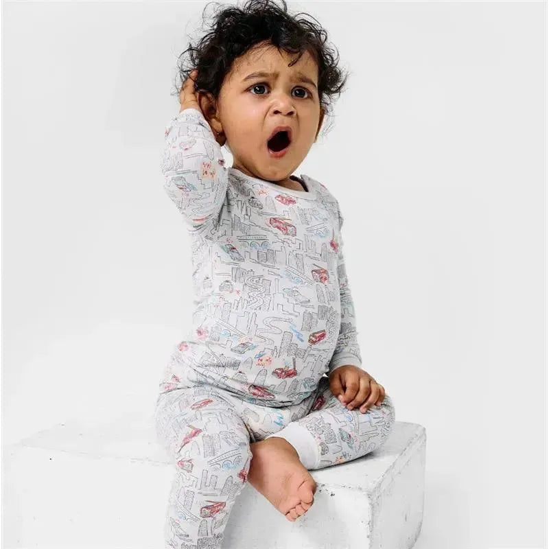 A young child in a long-sleeve pajama set featuring a cityscape design yawns while sitting on a white block.