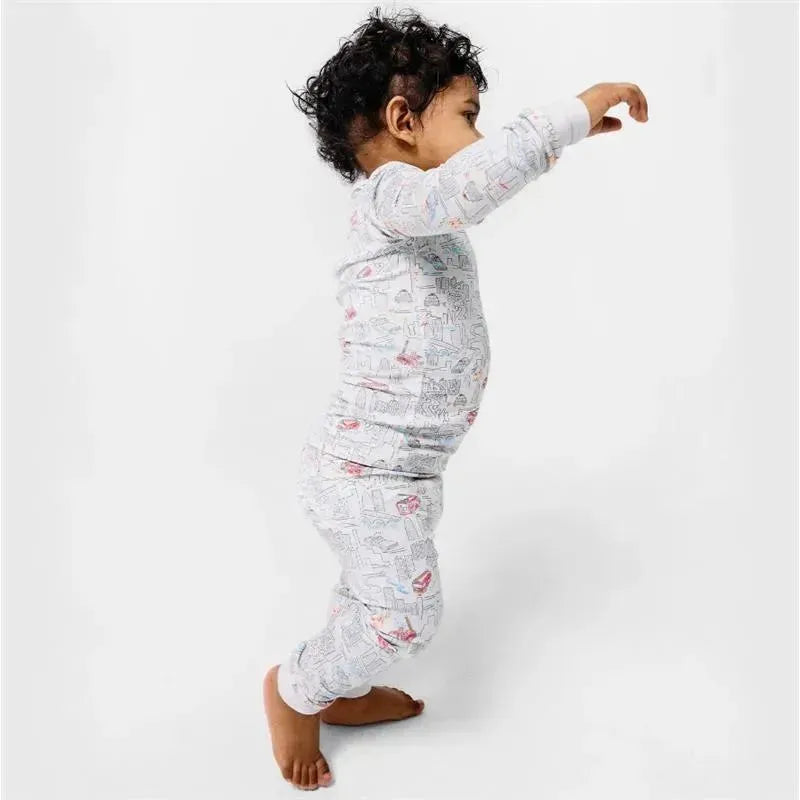 Toddler wearing a long sleeve pajama set with a cityscape design, playfully reaching out.