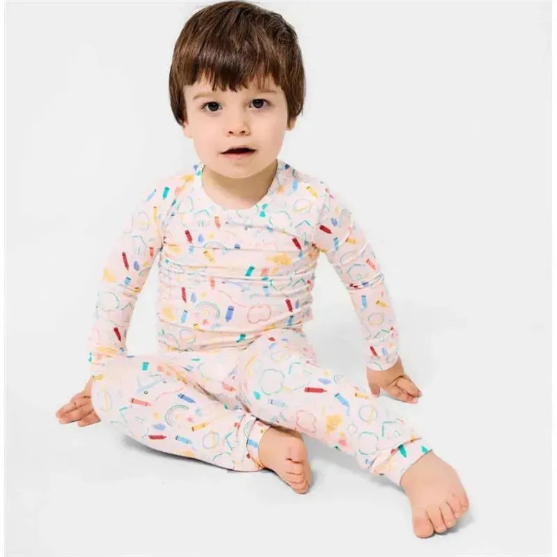A child sits cross-legged wearing a long-sleeve pajama set decorated with colorful doodles on a light background.