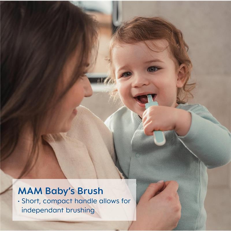 A toddler with curly hair holds a MAM baby toothbrush with a short handle, smiling while an adult looks on lovingly.