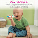 Toddler with a blue and white MAM baby toothbrush, smiling and practicing brushing teeth in a bright bathroom setting.