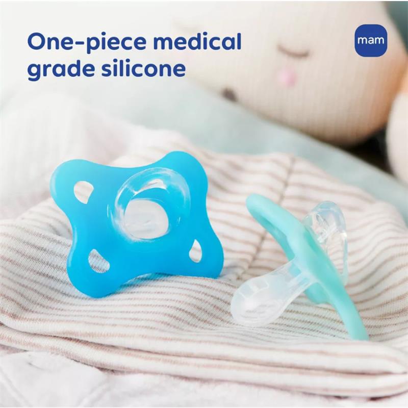 Two Mam pacifiers in assorted colors made of one-piece medical grade silicone, resting on a striped fabric surface.