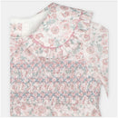 Smocked baby girl romper in woven fabric featuring a floral design with ruffled collar and pink tones.