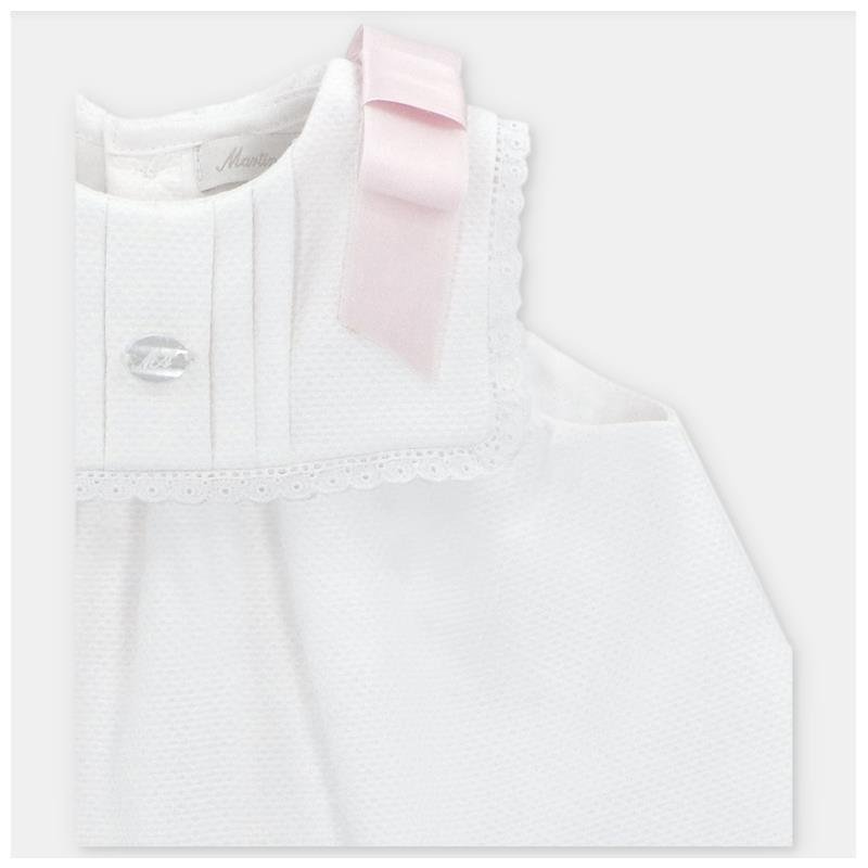 White baby dress with a pink ribbon on the shoulder and decorative scalloped edges, featuring a small crystal button.