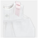 White baby dress with a pink ribbon on the shoulder and decorative scalloped edges, featuring a small crystal button.