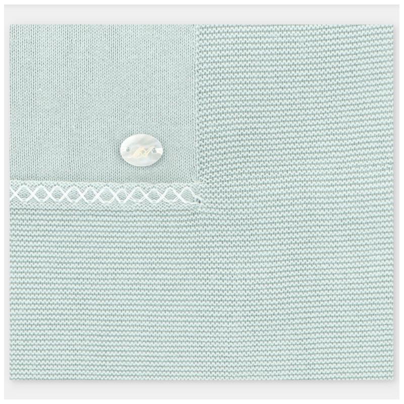 Light pink knit blanket featuring a decorative button and intricate stitching detail.