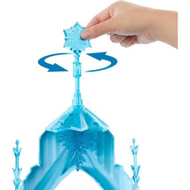 A hand is turning a snowflake-shaped top on the Mattel Disney Frozen Elsa Ice Castle playset, showcasing its blue structure.