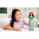 A young girl smiles while playing with a Mattel Disney Princess Ariel fashion doll, dressed in a turquoise outfit.