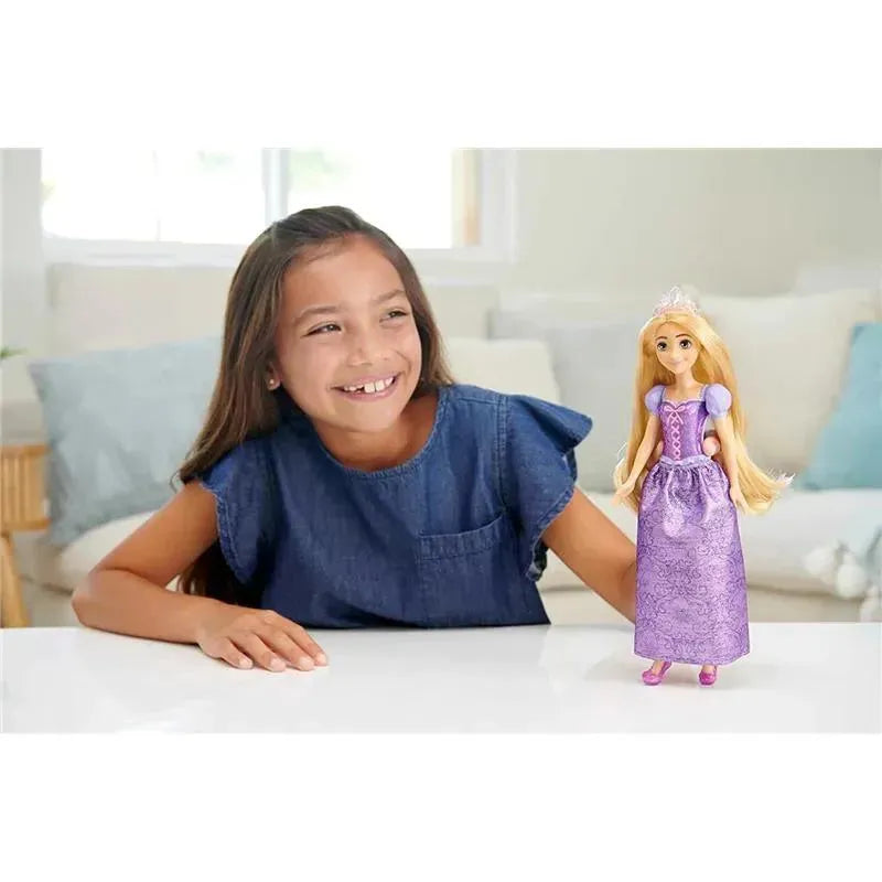 A girl smiles while playing with a Mattel Disney Princess Rapunzel fashion doll dressed in a purple gown with a tiara.