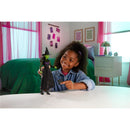 A young girl smiles and points at a Wicked Core Doll of Elphaba, depicting the character in a black dress and witch hat.