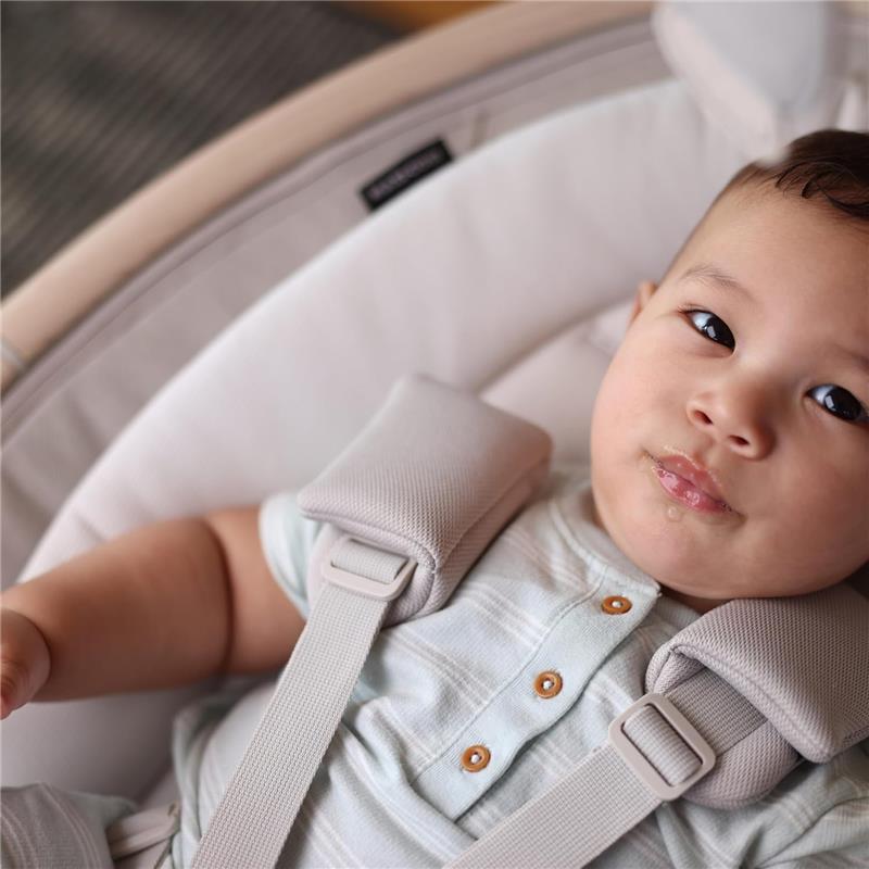 Infant resting in the Maxi-Cosi Cassia Smart Baby Swing, wearing a light blue shirt with buttons, secured in a soft, cushioned seat.