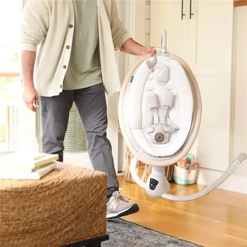 A person carrying a Maxi-Cosi Cassia Swing in Classic Green, featuring a padded seat and safety harness, in a bright room.