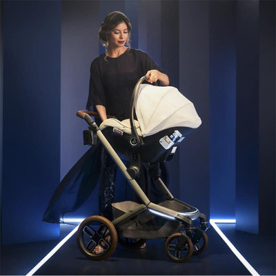 Woman adjusting a Maxi-Cosi Fame Modular Stroller in Twillic Truffle color, showcasing modern design against a dark background.