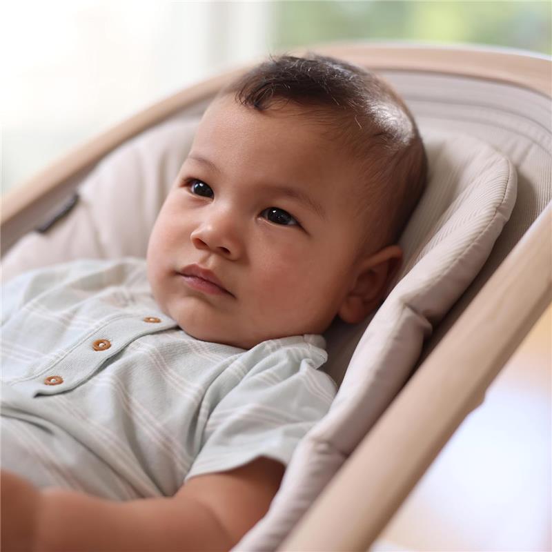 Baby in a Maxi-Cosi Kori 2-in-1 Baby Bouncer Seat, wearing a light blue outfit, looking thoughtfully.