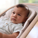 Baby in a Maxi-Cosi Kori 2-in-1 Baby Bouncer Seat, wearing a light blue outfit, looking thoughtfully.
