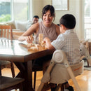 Mother and child playing a game with wooden blocks at a dining table, child seated in a Maxi-Cosi Minla high chair.