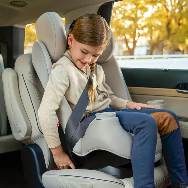 A young girl in a beige sweater sits securely in a Maxi-Cosi Pria All-in-One Convertible Car Seat, buckling her seatbelt.