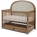 Maxi Cosi Quiet Luxury 6-in-1 convertible crib with a natural wood finish, upholstered headboard, and a storage drawer below.