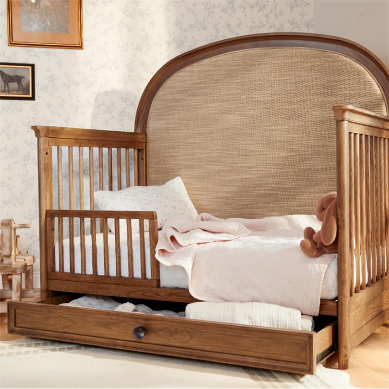 Maxi Cosi Quiet Luxury 6-in-1 Convertible Crib featuring a wooden frame, plush bedding, and a storage drawer below.