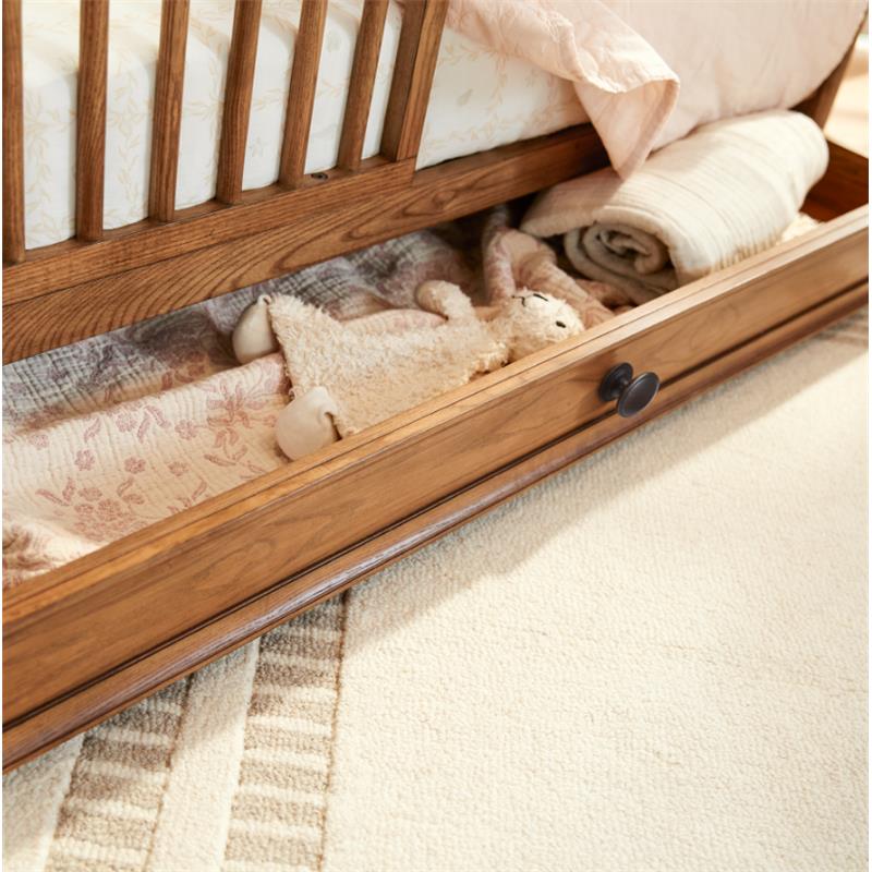 Maxi Cosi Quiet Luxury 6-in-1 Convertible Crib showing a storage drawer with a plush toy, blankets, and a patterned covering.