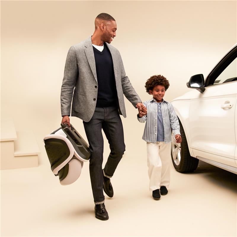 A father holds hands with his son while carrying a Maxi-Cosi Tanza folding booster car seat in Sea Shadow color.