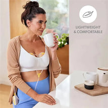 Hands-free breast pump collection cups with tubing displayed on a woman in a white bra, sipping from a coffee mug at home.