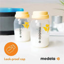 Two Medela breast milk collection and storage bottles with yellow leak-proof caps, filled with milk, on a light surface.