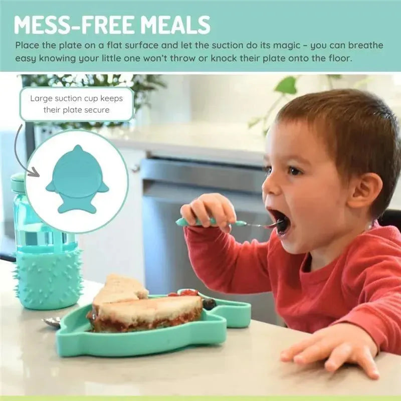 A child with short brown hair eating from a blue shark-shaped silicone suction plate, featuring a sandwich and berries.