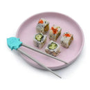 Chopsticks designed as a shark, next to sushi rolls on a pink plate, highlighting the playful training aspect of the product.
