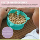 Silicone suction bowl in shark blue filled with cereal, held by a child encouraging self-feeding and fine motor skills.