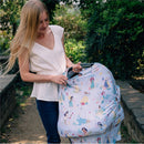 A woman adjusts a colorful Milk Snob 5-in-1 cover featuring Disney princesses over a stroller in an outdoor setting.