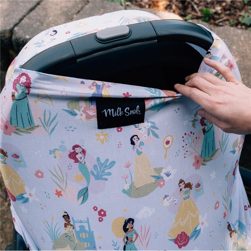 Multifunctional cover by Milk Snob featuring Disney princesses in colorful prints, being adjusted on a car seat.