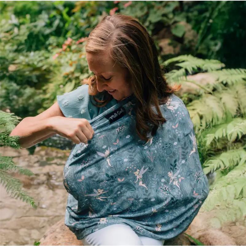 A woman in a blue shirt uses a Tinker Bell-patterned multifunctional cover, smiling as she adjusts it while surrounded by greenery.