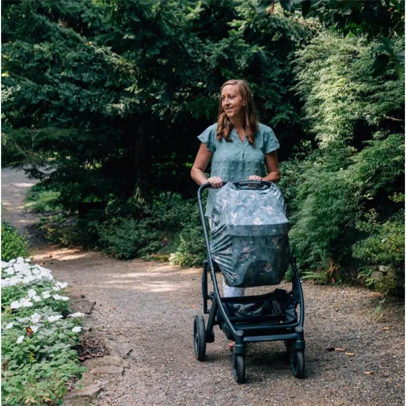 A woman pushes a stroller covered with a Milk Snob Tinker Bell multifunctional cover while walking on a garden path.