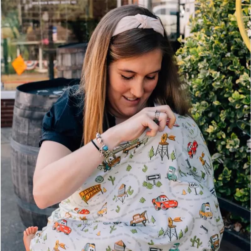 Woman using a Milk Snob Disney and Pixar multifunctional cover featuring a Cars design, smiling while adjusting the fabric.