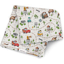 Milk Snob Cars swaddle blanket featuring colorful illustrations of cars, roads, and landmarks on a light background.