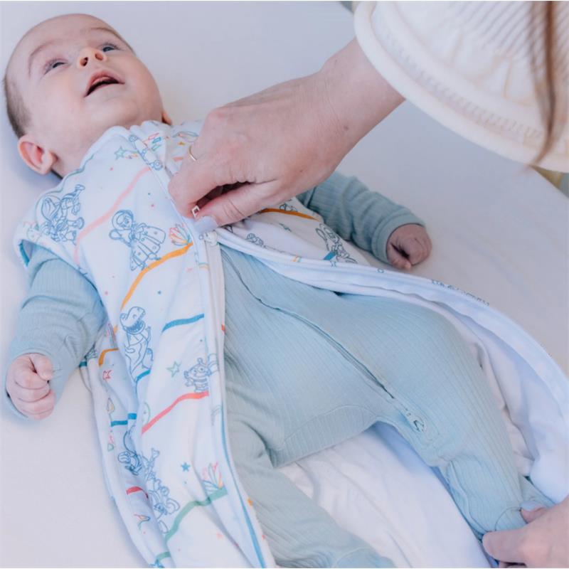 Baby in a Disney Pixar Toy Story sleep bag, being zipped up by a caregiver, smiling. The sleep bag features colorful character illustrations.