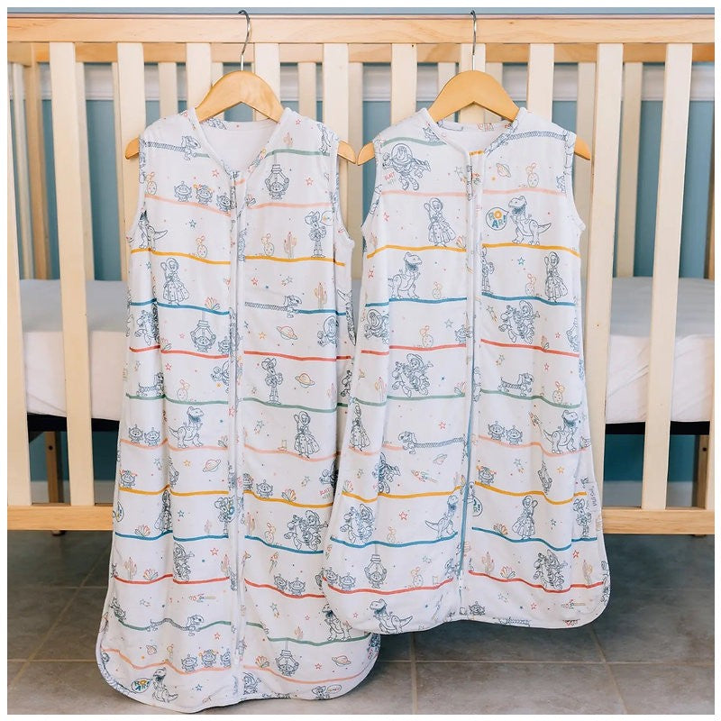Milk Snob Disney Pixar Toy Story baby sleep bags, featuring colorful cartoon characters, hanging in front of a crib.