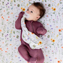 Baby lying on a floral-patterned blanket, holding a Milk Snob Eloise Lovey security blanket and a pacifier.