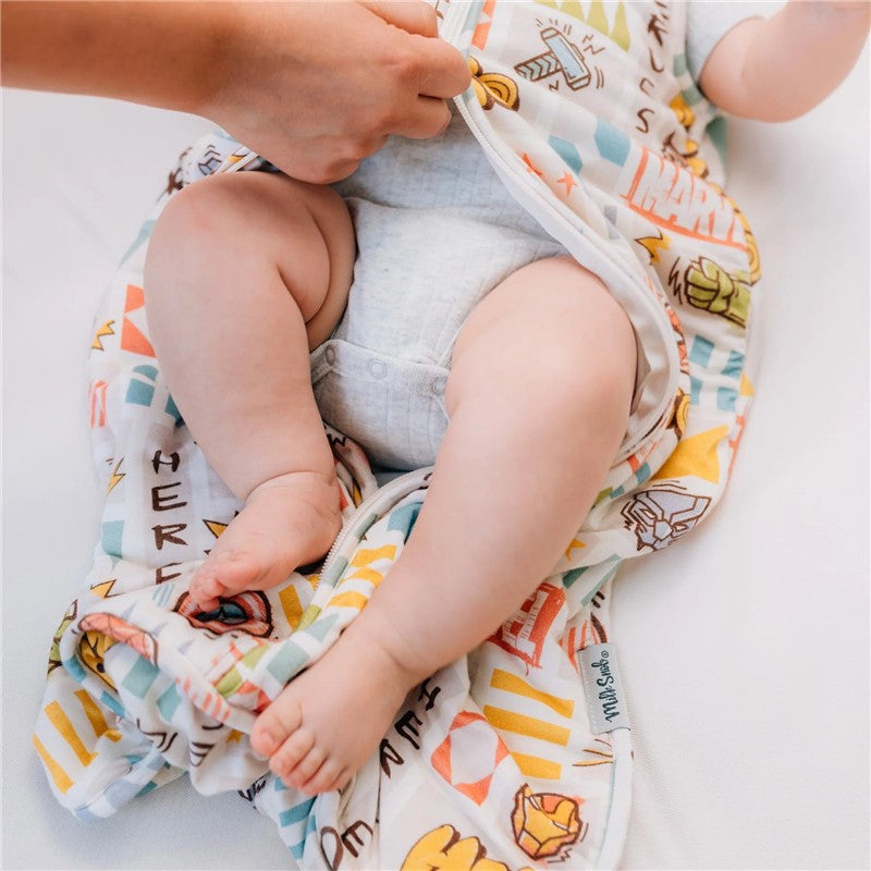 Milk Snob Marvel World Baby Sleep Bag shown being zipped up around a baby, featuring colorful superhero designs.