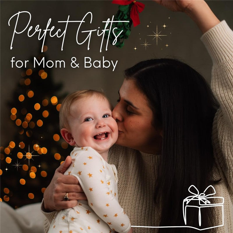 Mother kisses her smiling baby wearing a star-patterned onesie, decorated Christmas tree in the background, with holiday text.