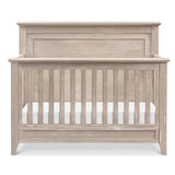 Rustic 4-in-1 convertible crib in sandbar finish, featuring a curved top and slatted front for safety.