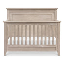 Rustic 4-in-1 convertible crib in sandbar finish, featuring a curved top and slatted front for safety.