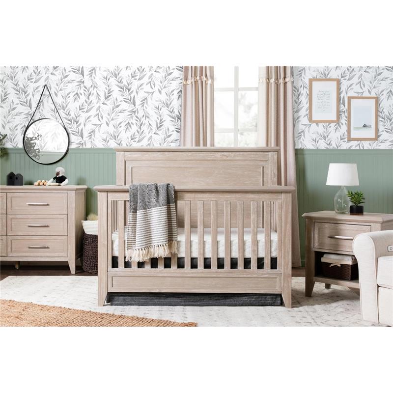 Rustic Million Dollar Baby Beckett 4-in-1 convertible crib in sandbar finish, with a cozy blanket, in a stylish nursery setting.
