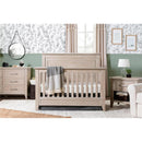 Rustic Million Dollar Baby Beckett 4-in-1 convertible crib in sandbar finish, with a cozy blanket, in a stylish nursery setting.